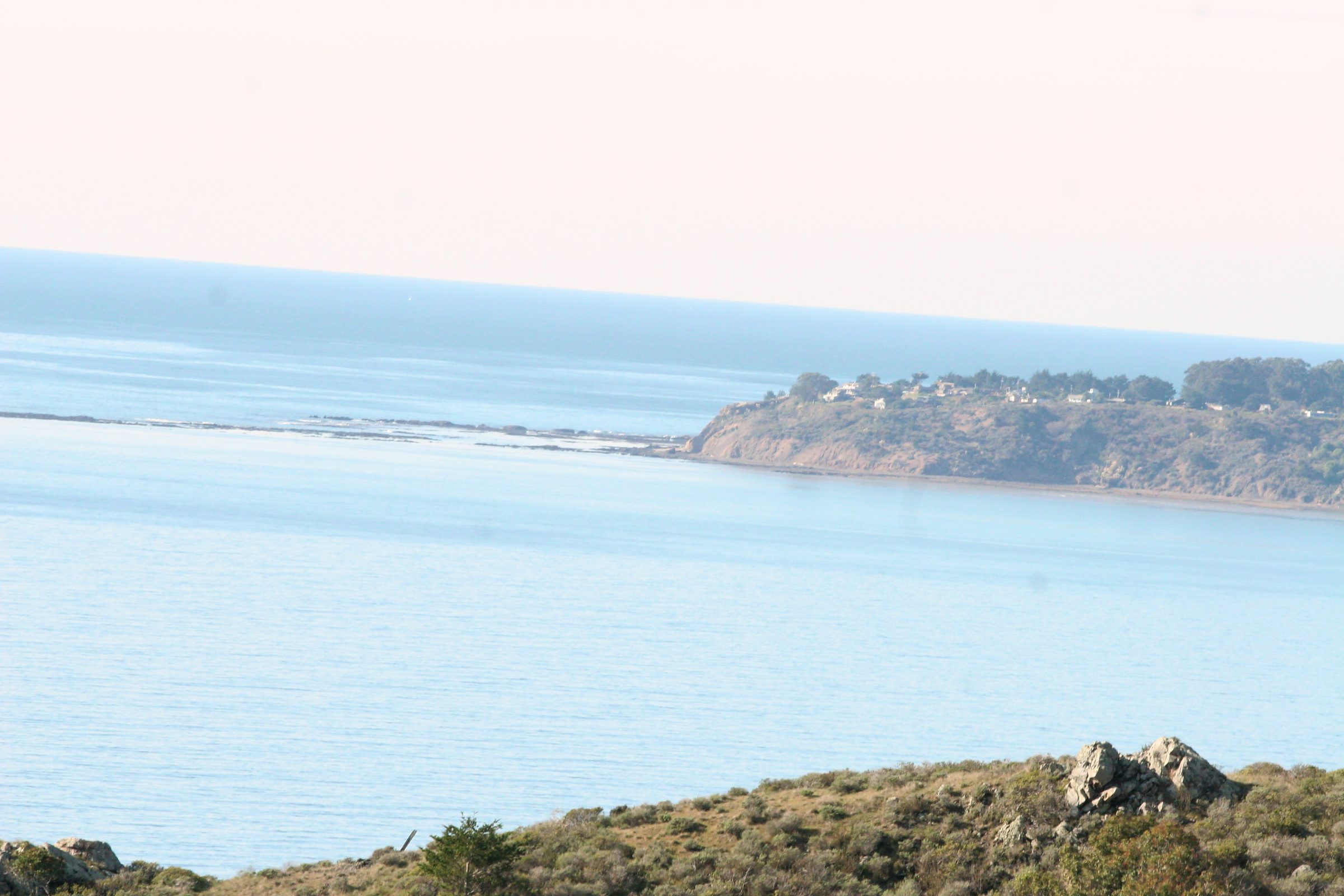 Pale blue water and rocky grassy shore with distant islets.
