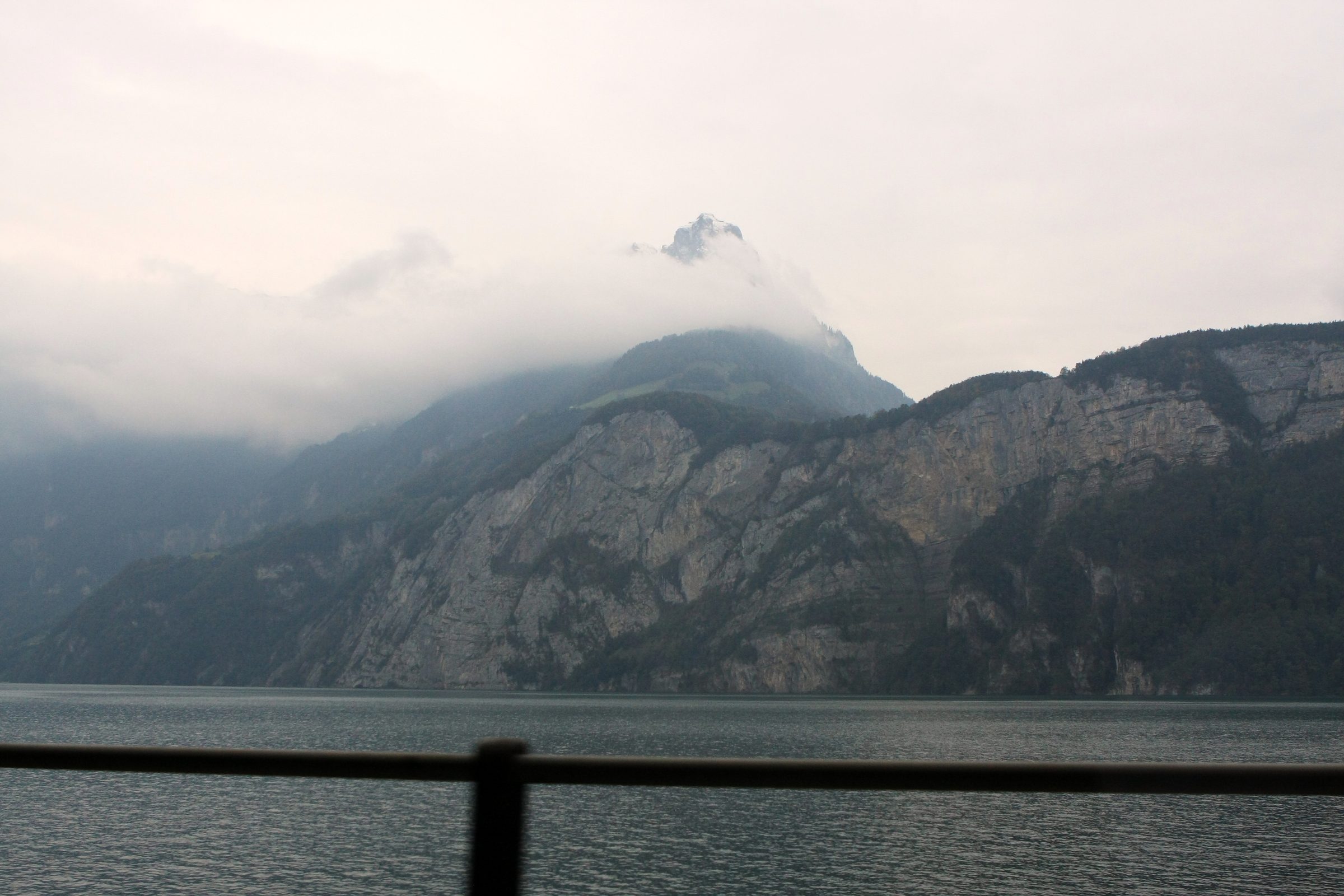 Metal railing overlooking a misty lake and rocky mountain.