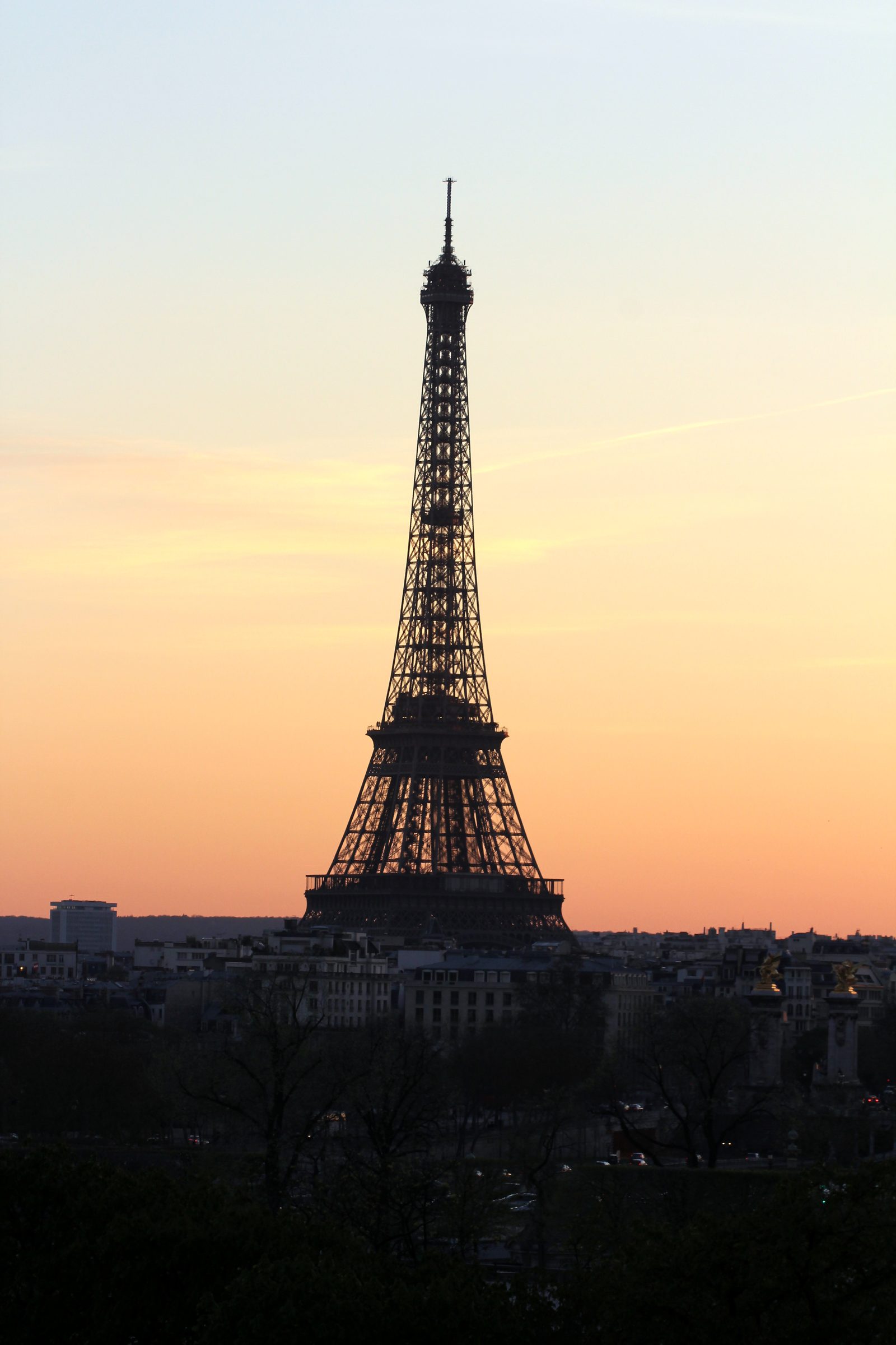 Eiffel Tower silhouette against pale apricot twilight sky.