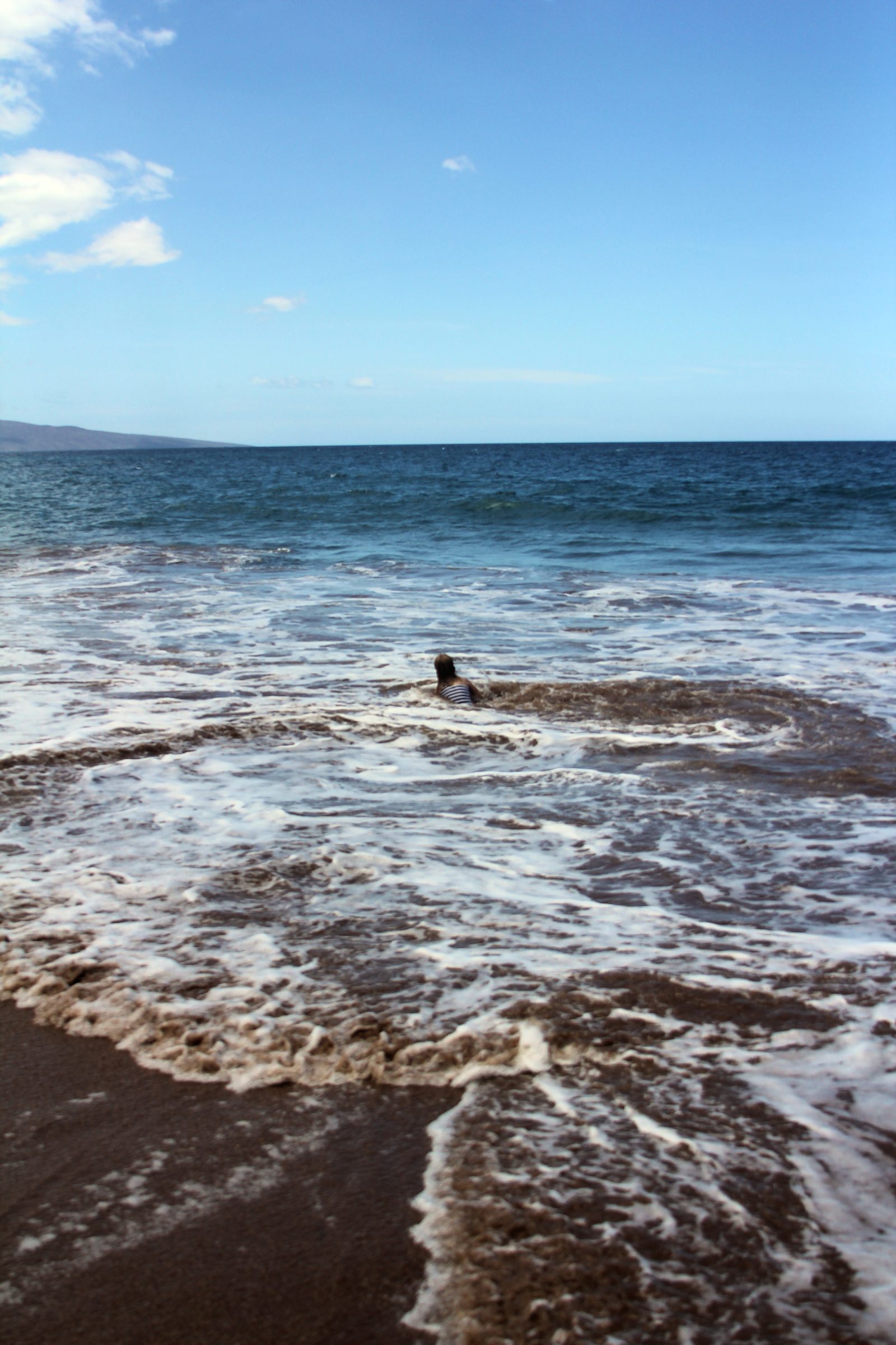 White foam washing over dark volcanic sand under blue sky.
