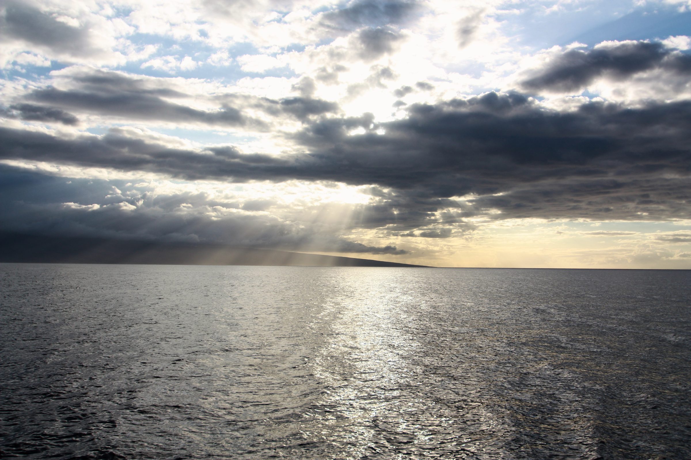 Silver sunlight fanning across dark water under textured clouds.