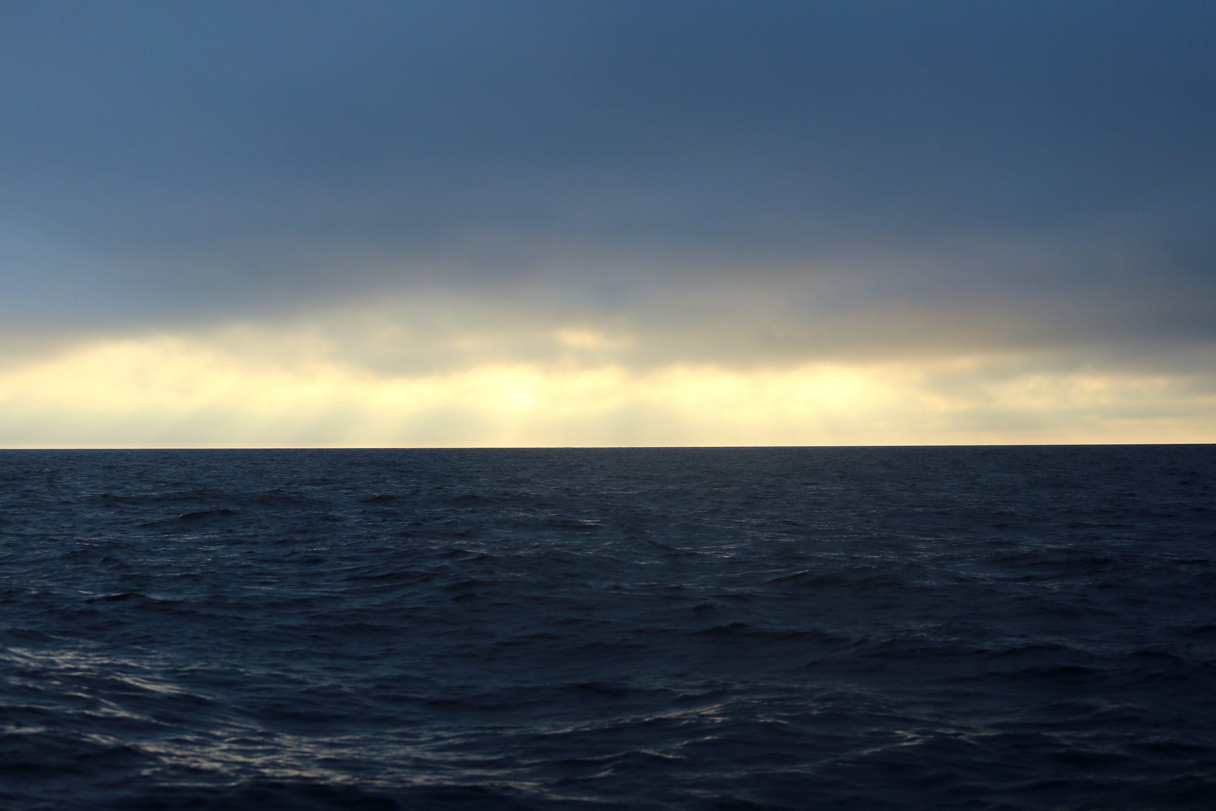 Dark stormy ocean with a bright cream band of light through clouds.