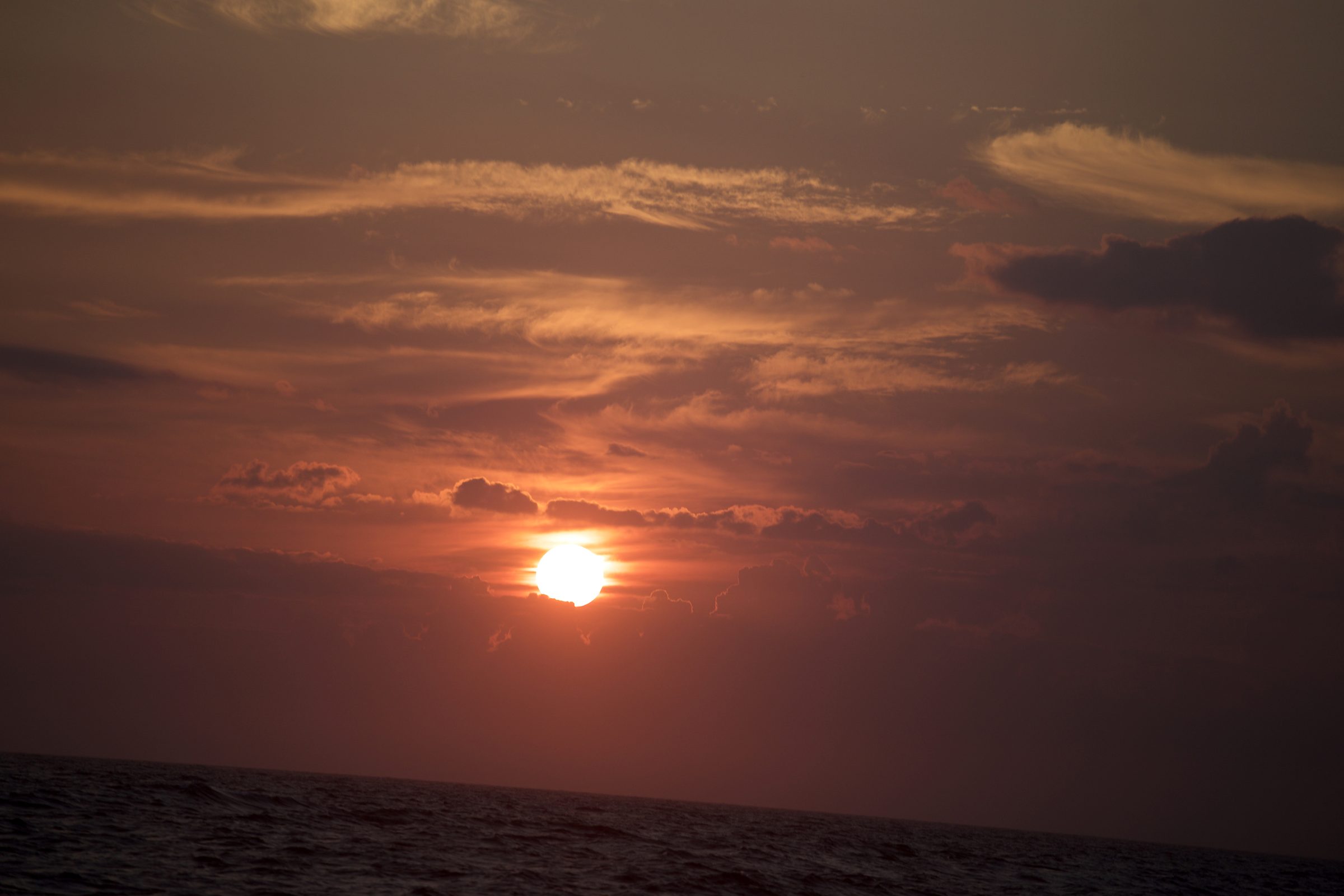Deep orange sunset orb low over a choppy dark sea.