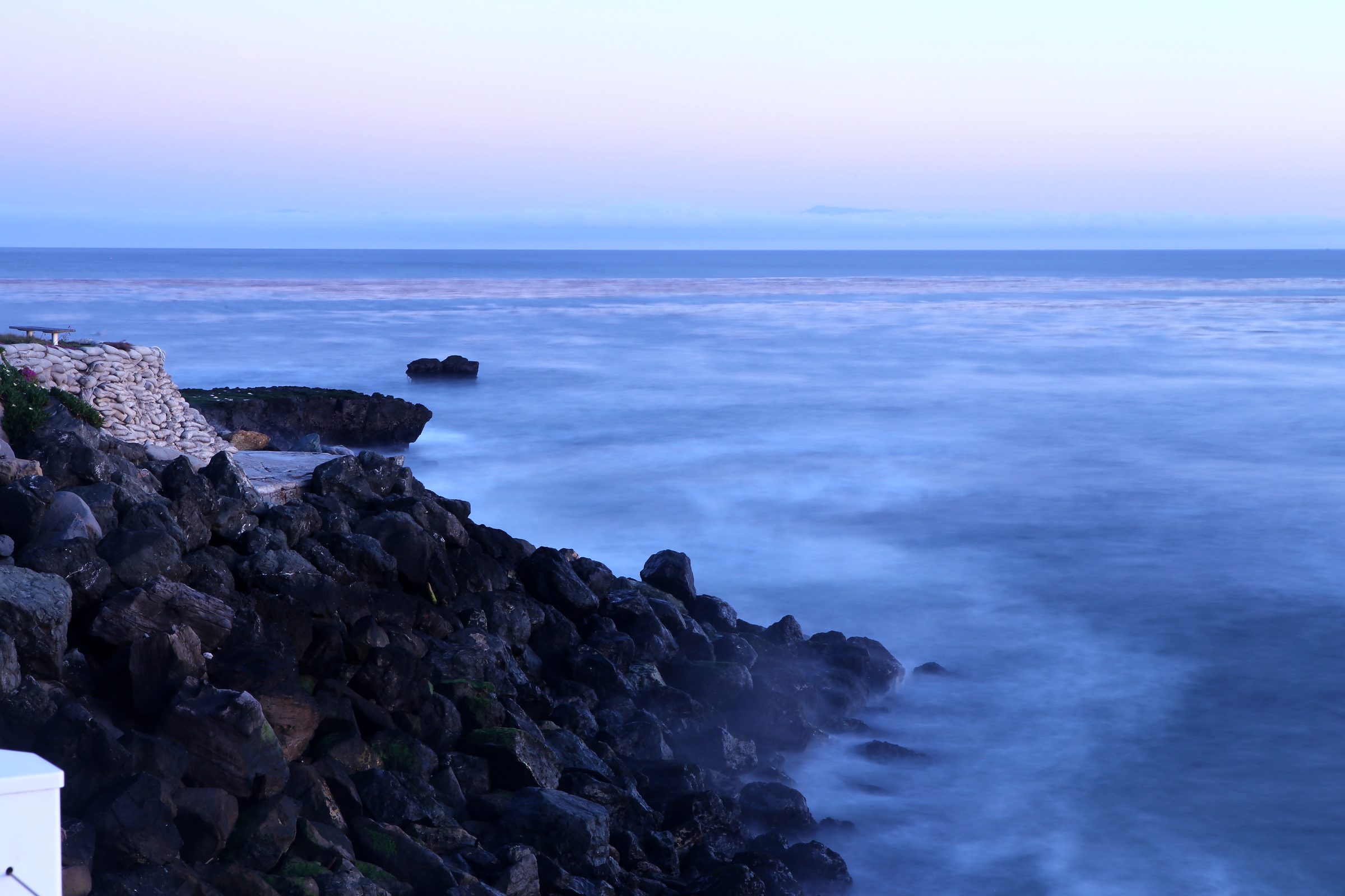 Long-exposure rocky coast with milky tide under purple-blue dusk.