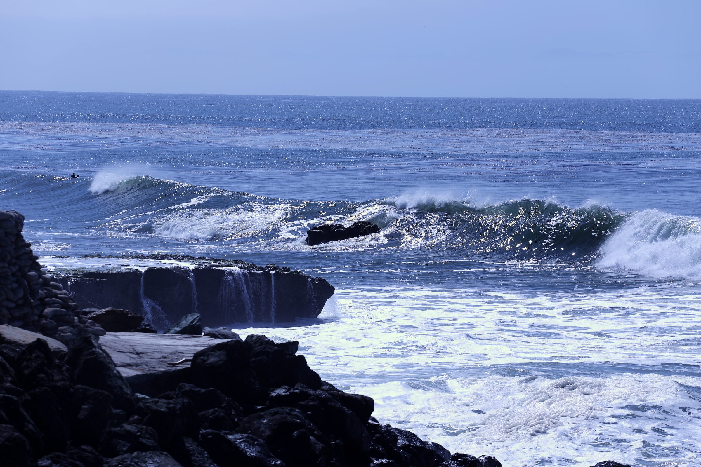Large wave cresting beside a flat rock shelf in white surf.