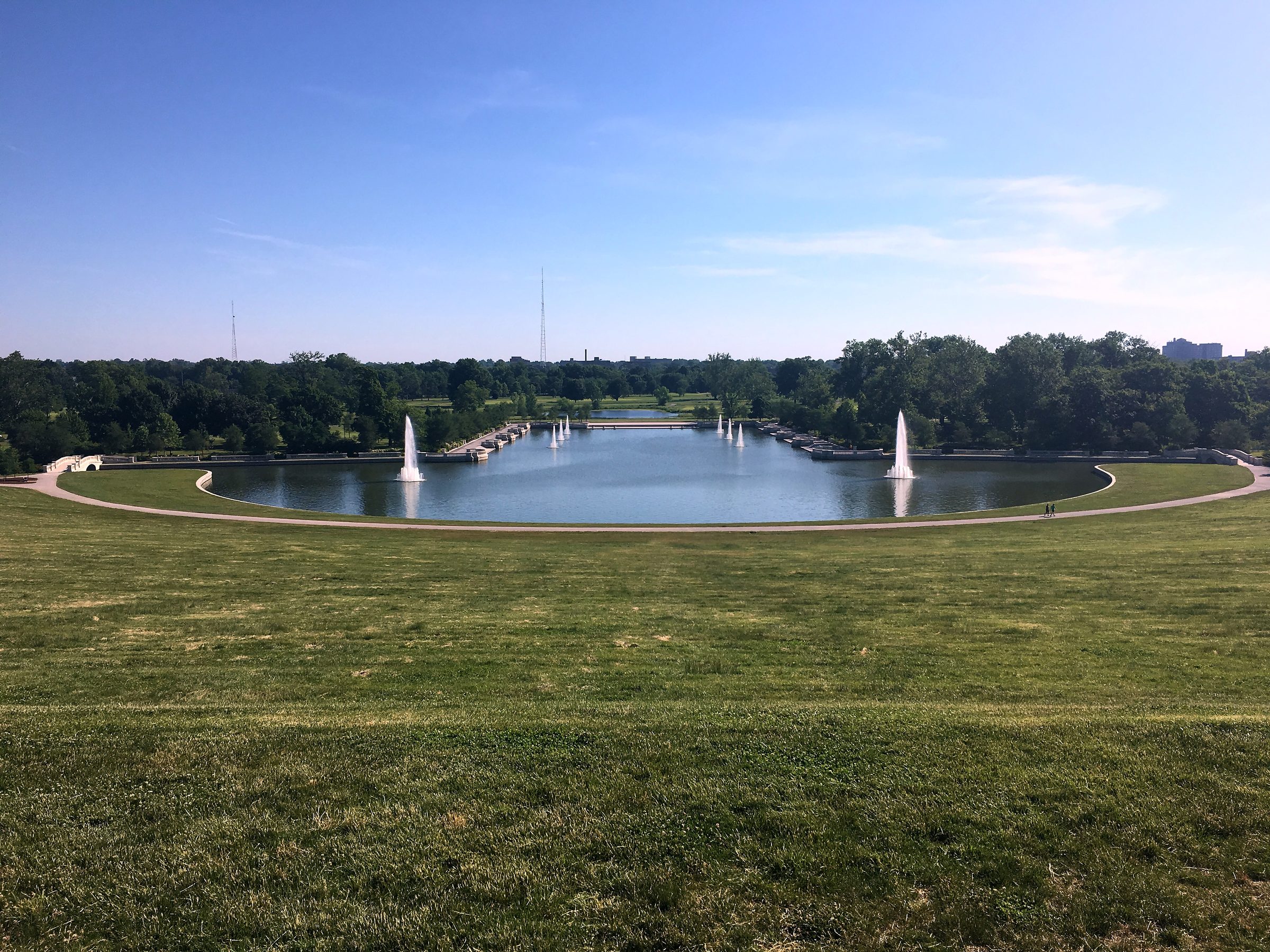 Long reflecting pool with fountains aiming at a distant hill building.