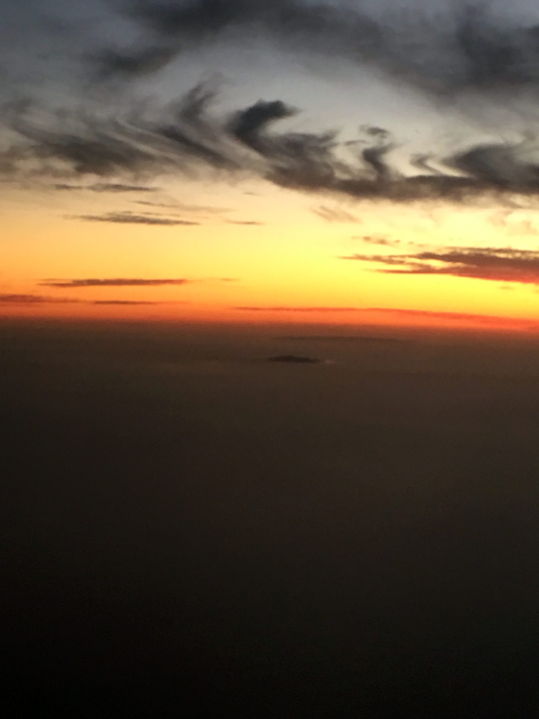 Vertical silhouette land against streaked orange-yellow sunset sky.