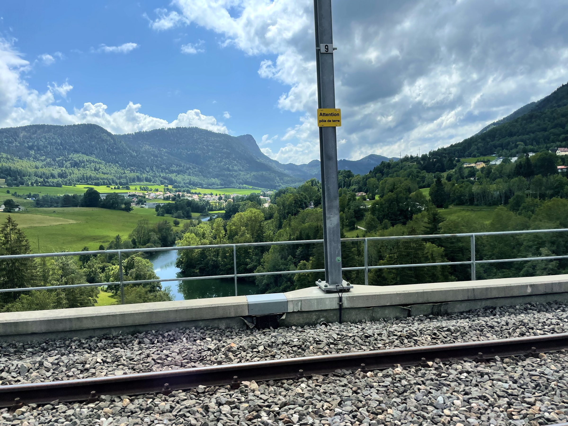 Train tracks overlooking a lush green valley and distant river.