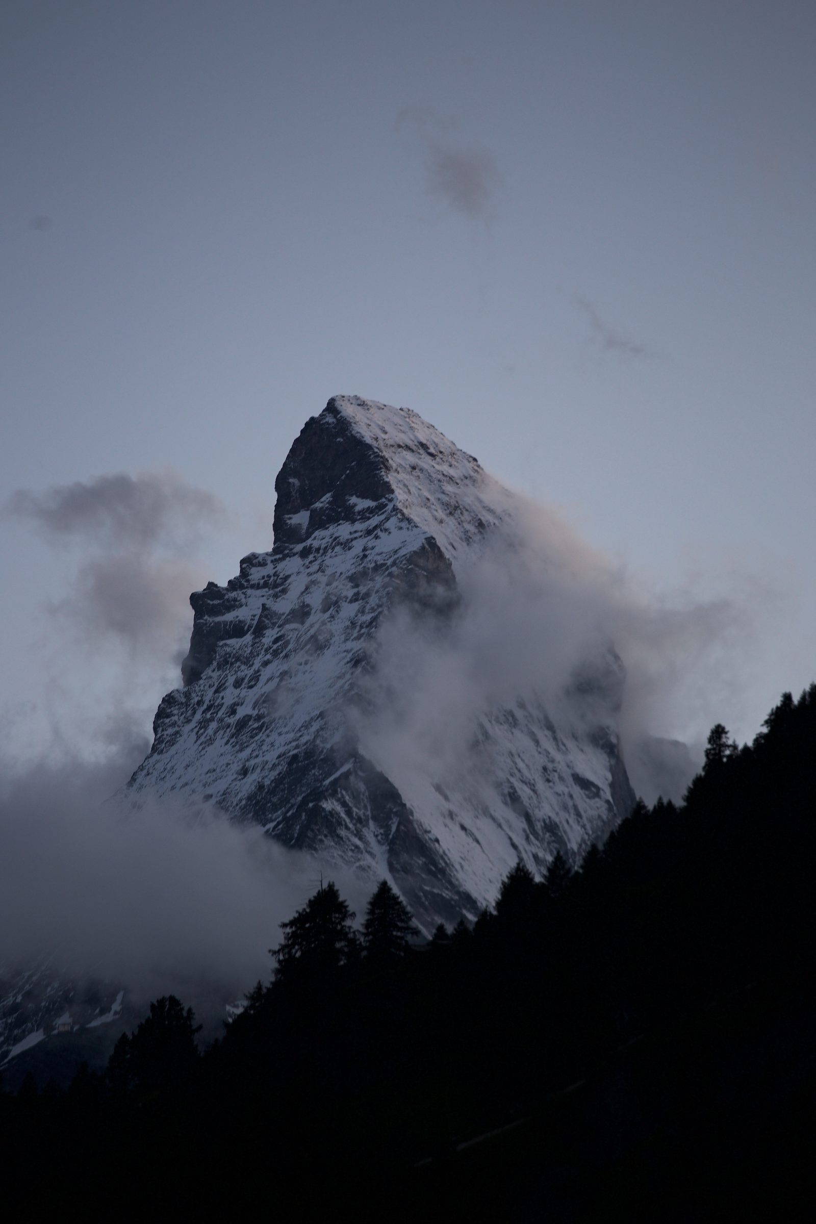 Moody Matterhorn pyramid alone in swirling grey cloud.
