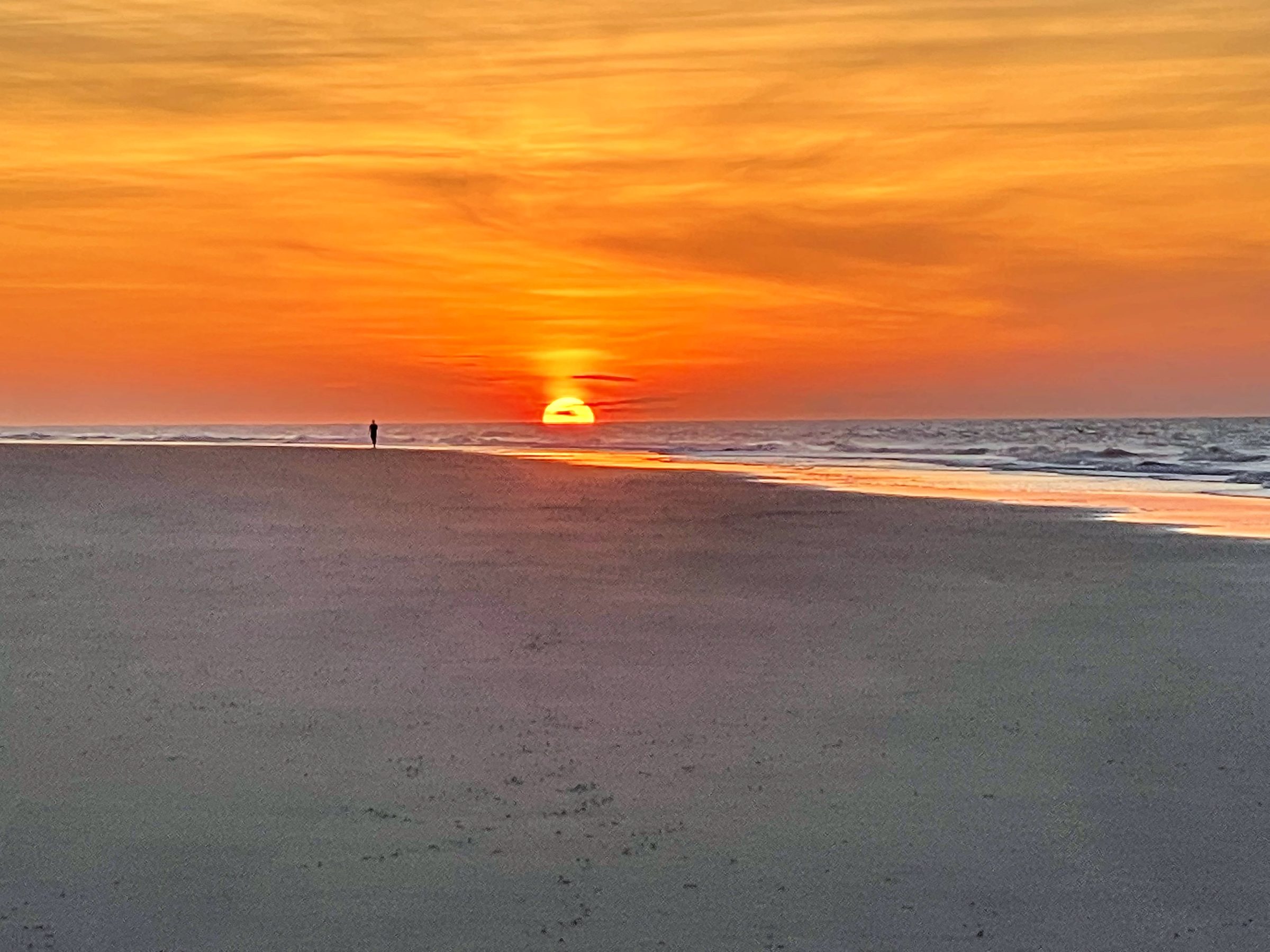 Bright orange sun on the horizon over wet flat sand.