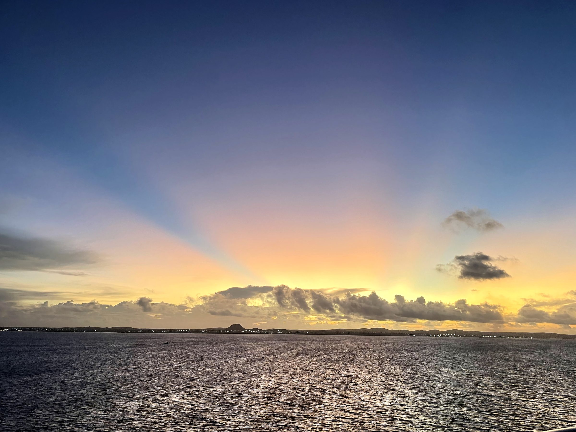 Fan-like yellow light rays rising into a purple twilight sea sky.
