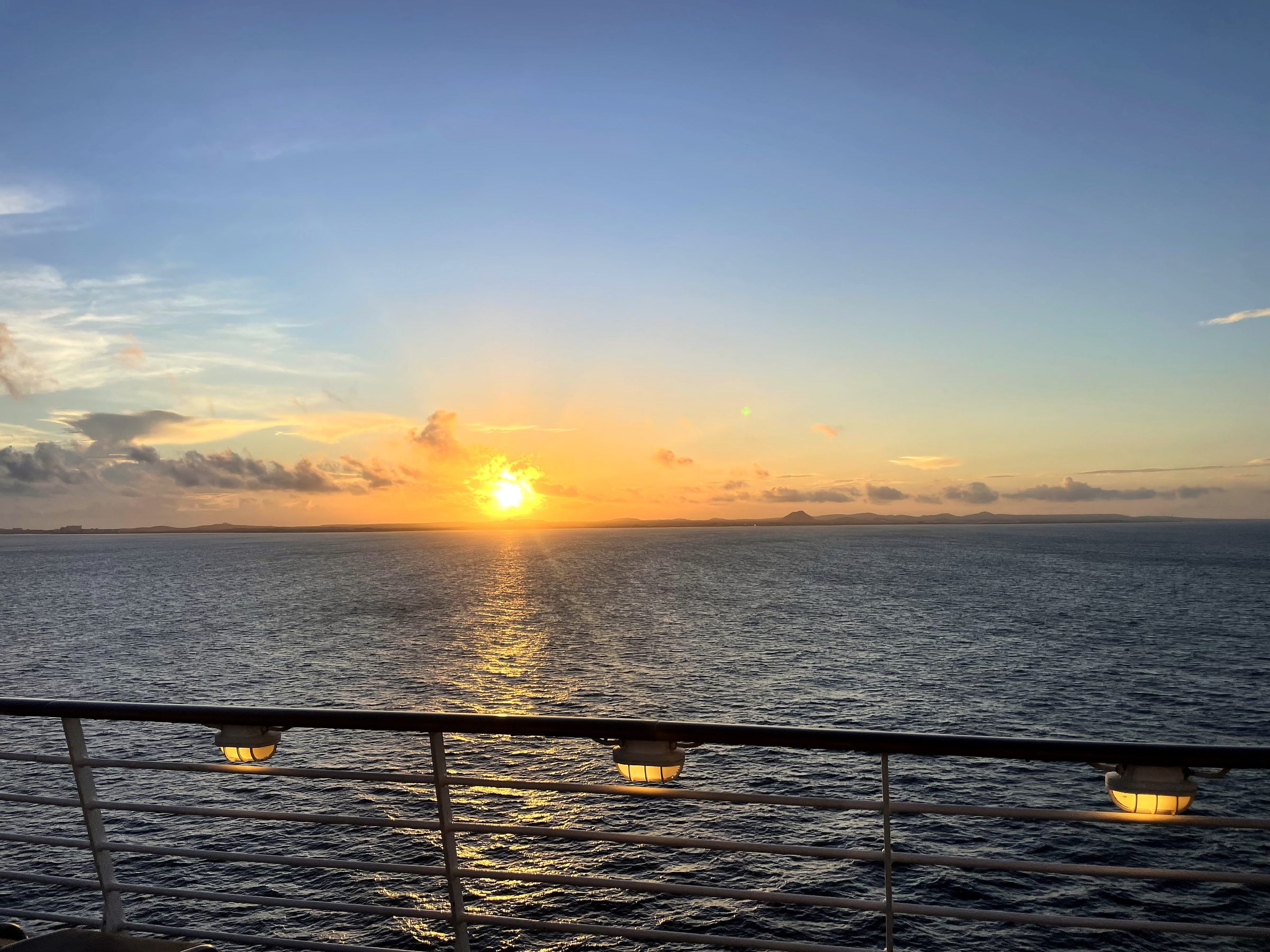 Ship-deck lamps above a gold sun path on the ocean.