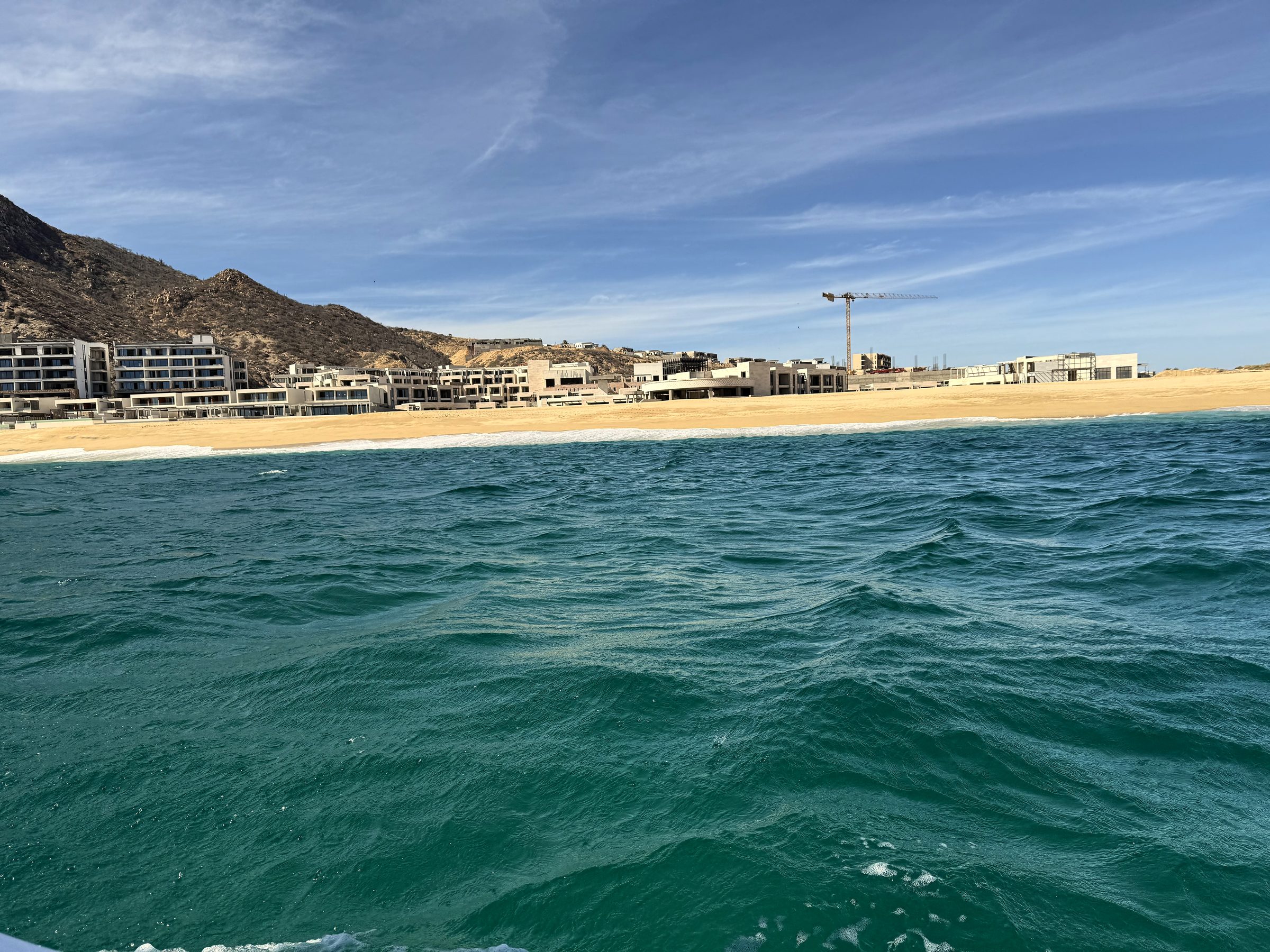 Turquoise water toward a beige resort shore with a tall crane.