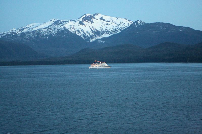 Small white ferry crossing a deep blue bay toward snowy mountains.