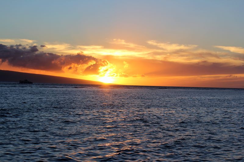 Bright sun touching the ocean horizon with a small boat silhouette.
