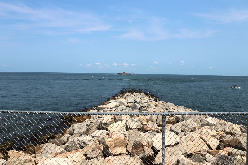 Stone jetty aiming at a small island across blue water.