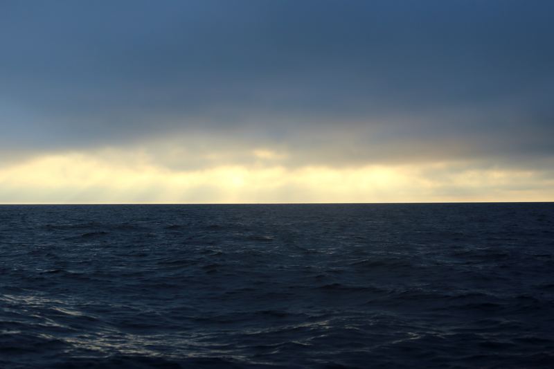 Dark stormy ocean with a bright cream band of light through clouds.