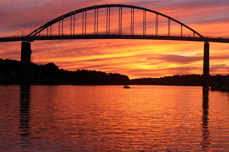 Arched bridge silhouetted against fiery orange sunset water.