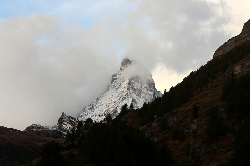 Snowy peak emerging from mist above a dark forested slope.