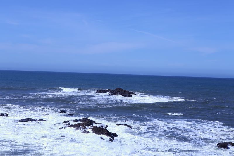 Rough blue ocean and white surf among dark coastal rocks.