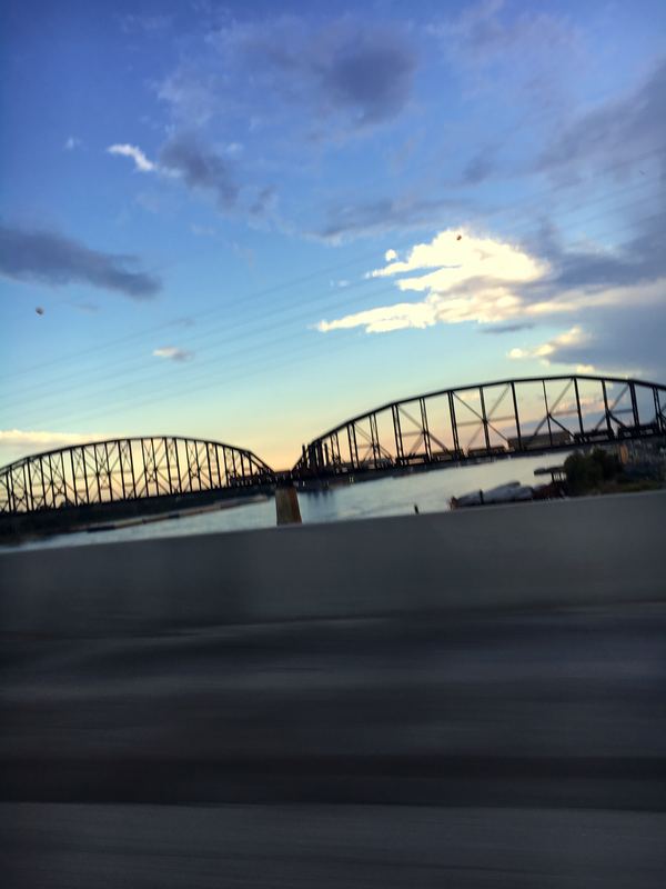 Blurred black iron truss bridge under streaky blue sky.