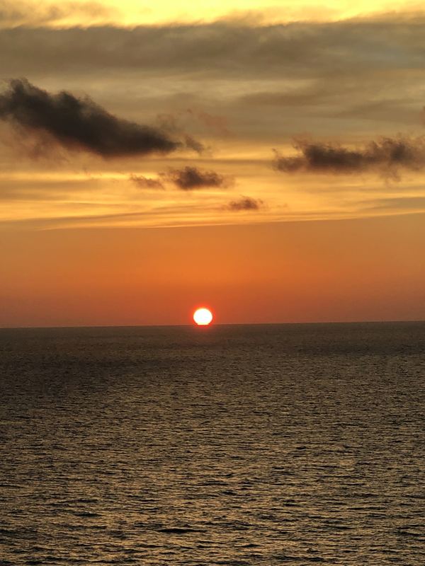 Vertical ocean sunset with orange sun centered on the horizon.