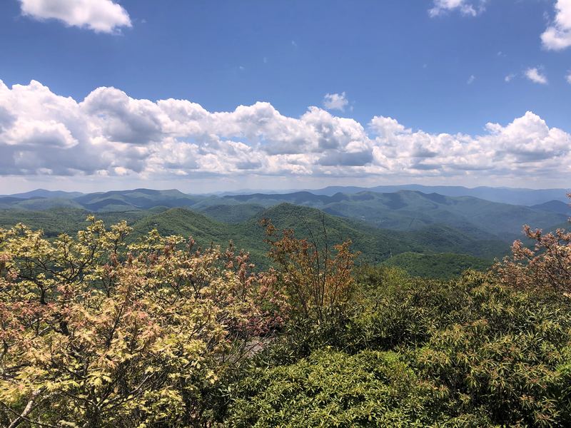 High vantage of stacked green ridges under blue sky and white clouds.