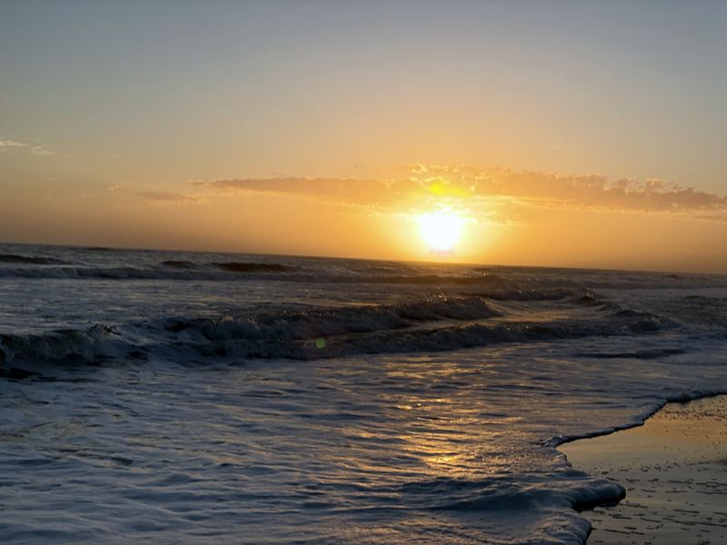 Low sun glaring gold over ocean waves and foam lace.