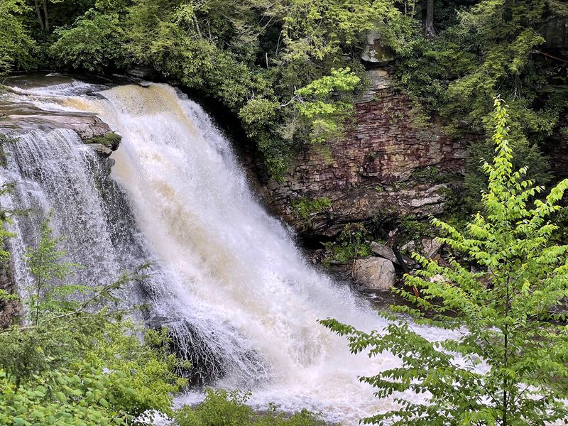 Wide waterfall curtain cascading before a reddish rock cliff.