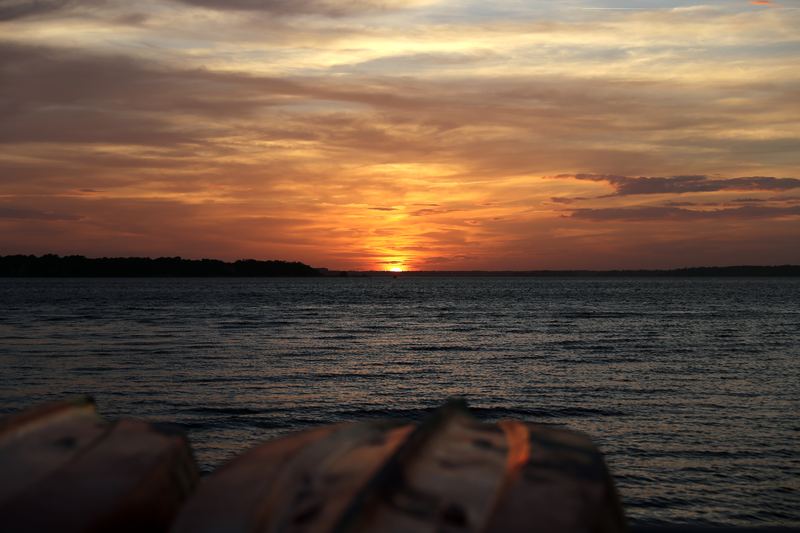 Moody orange sunset over water framed by overturned boat hulls.