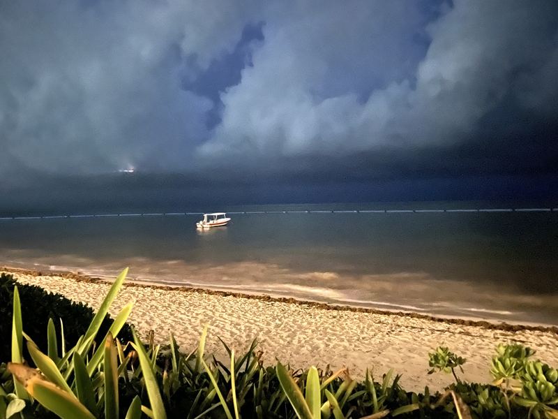 Small white boat under heavy dark storm clouds by the shore.