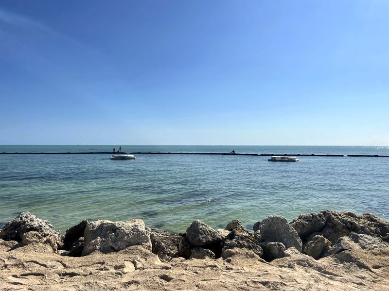 Rocky riprap shore with twin swim rafts on clear turquoise water.