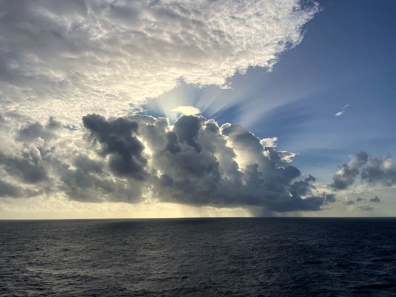 Sunbeams and rain streaks through a haloed cloud over sea.