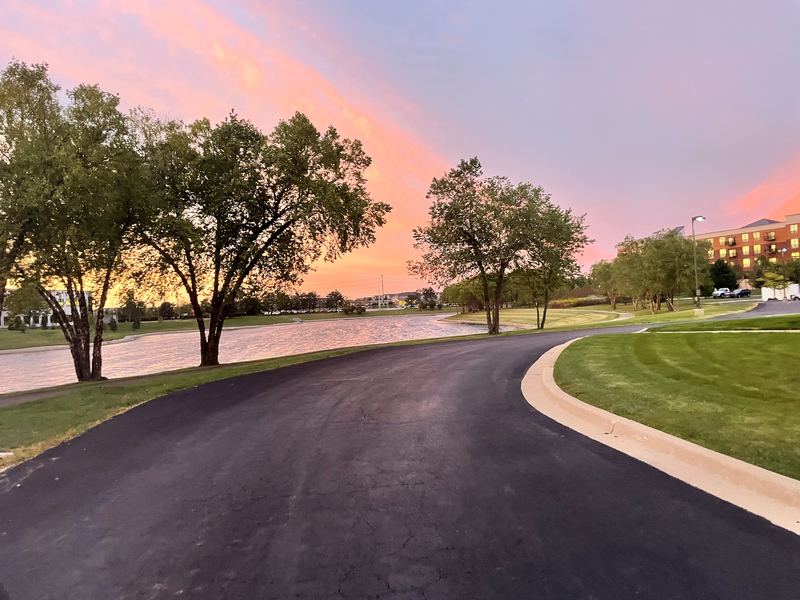 Park path curving beside water into a pink-violet sunset.