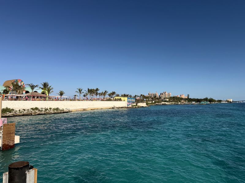 White seawall into turquoise water toward distant towers and palms.