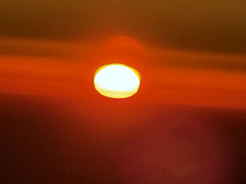 Close-up of a large smoky amber sun disk in hazy sky.
