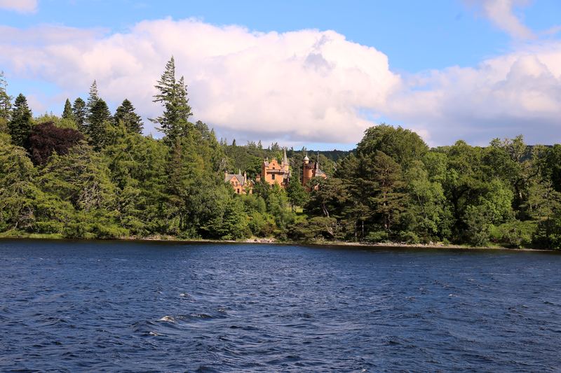 Calm Scottish loch with forest shore and a pinkish manor hint.