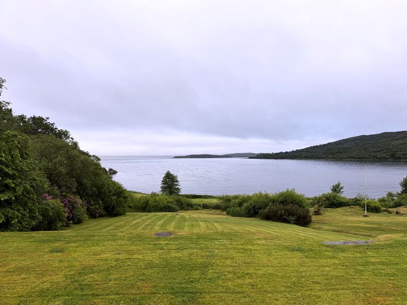 Striped green lawn leading to a silver bay under overcast sky.